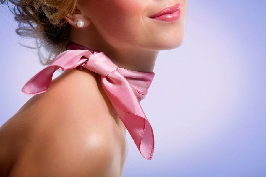 Woman wearing creative hair scarf styled as elegant neck bow with pearl earrings