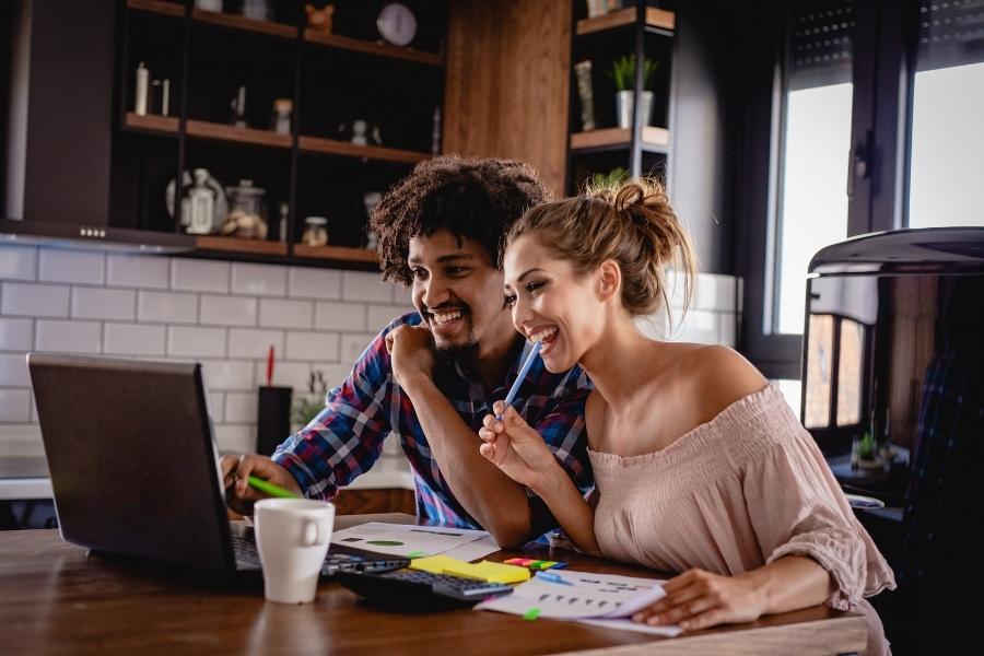 Happy couple planning budget minimalist wedding decor at kitchen table with laptop and documents
