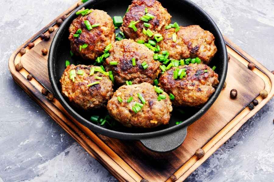 Golden-brown meatballs cooked in a well-seasoned cast iron skillet with fresh green onions