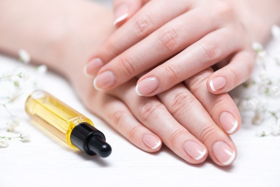 Hands with healthy nails next to cuticle oil bottle for nail care routine