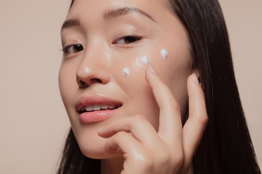 Woman applying Korean Glass Skin skincare cream to achieve dewy complexion