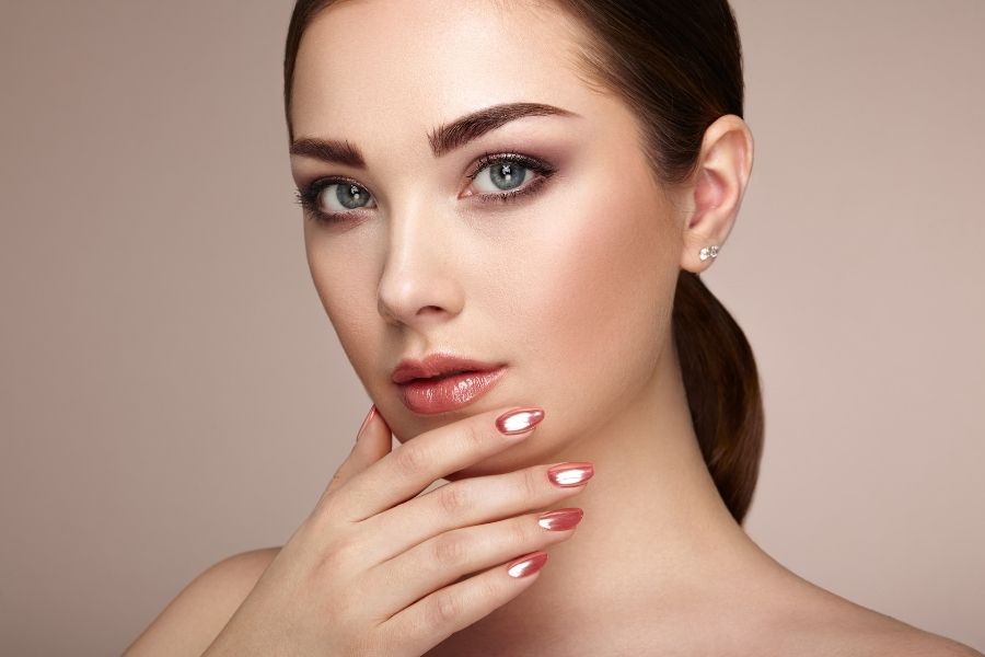 Woman showcasing perfect makeup application with natural glowing skin and coral tones