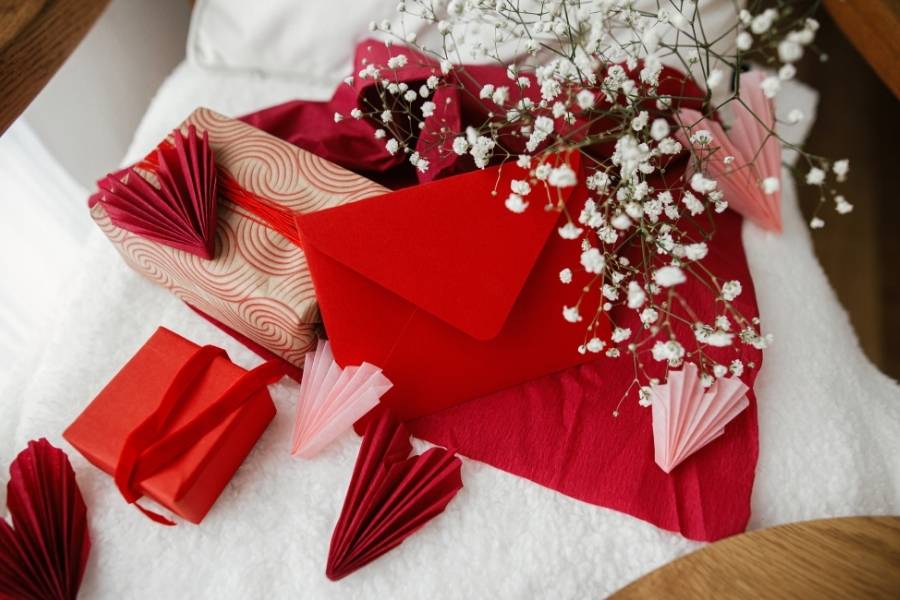Handmade Valentine gift supplies including red paper fans, gift boxes, and baby's breath flowers arranged on white fabric