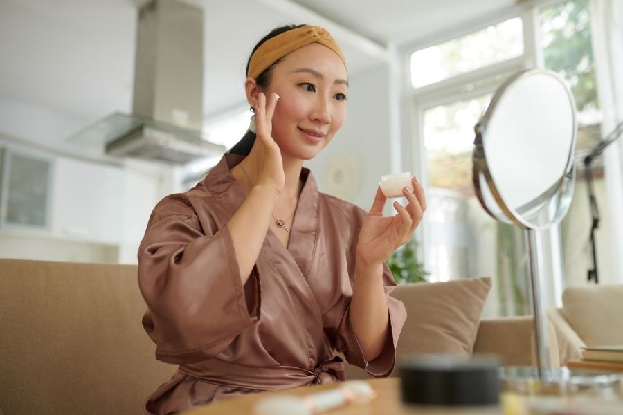 Woman applying anti-aging skincare routine products while looking in mirror at home