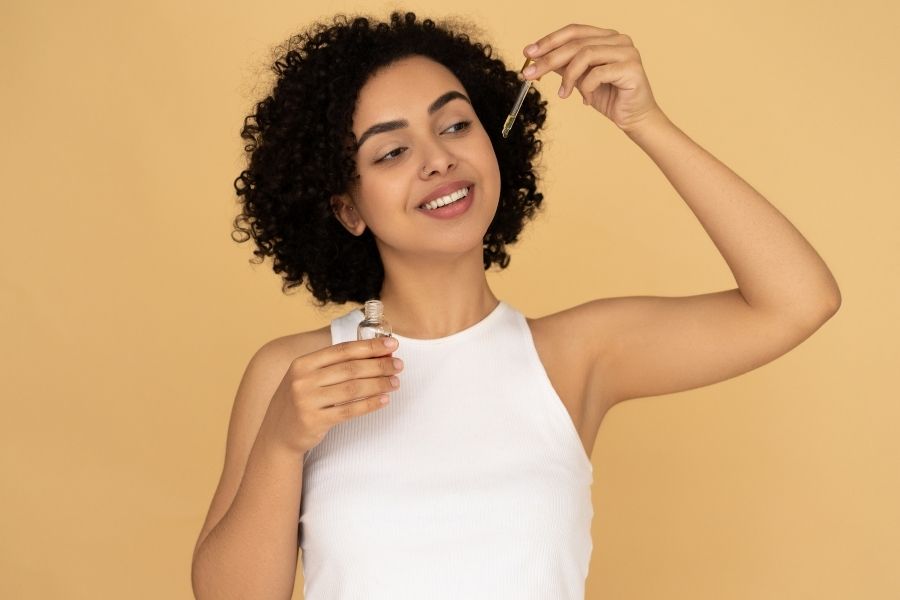 Woman applying beauty hacks with facial serum using dropper against warm yellow background