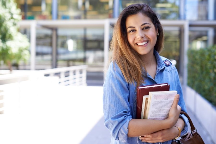 Happy female student holding books outdoors with bright, radiant eyes and a warm smile