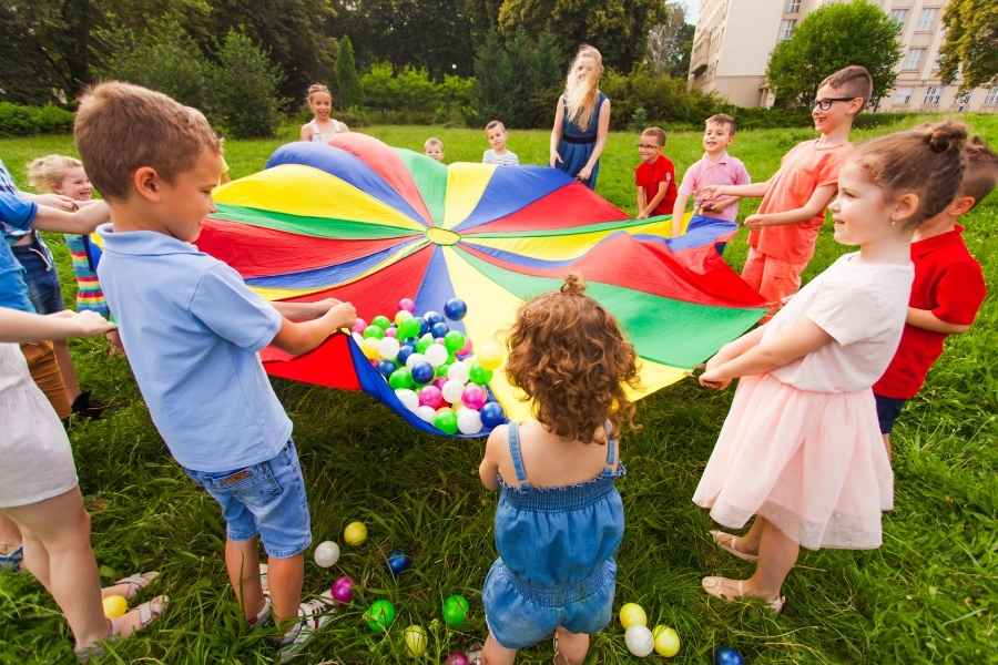 Children enjoying creative activities with colorful parachute game and balls in outdoor setting