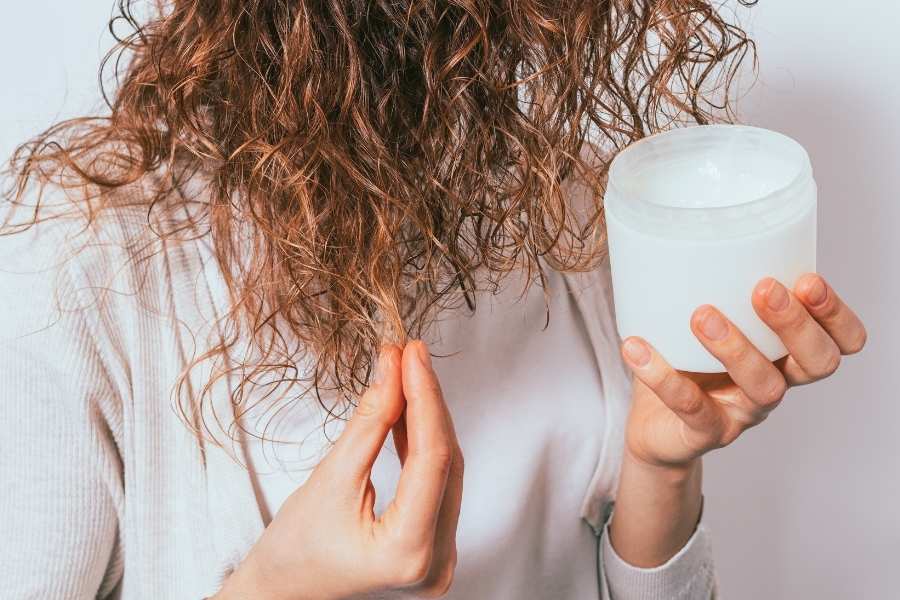 Woman with wet curly hair applying curly hair care product from white container