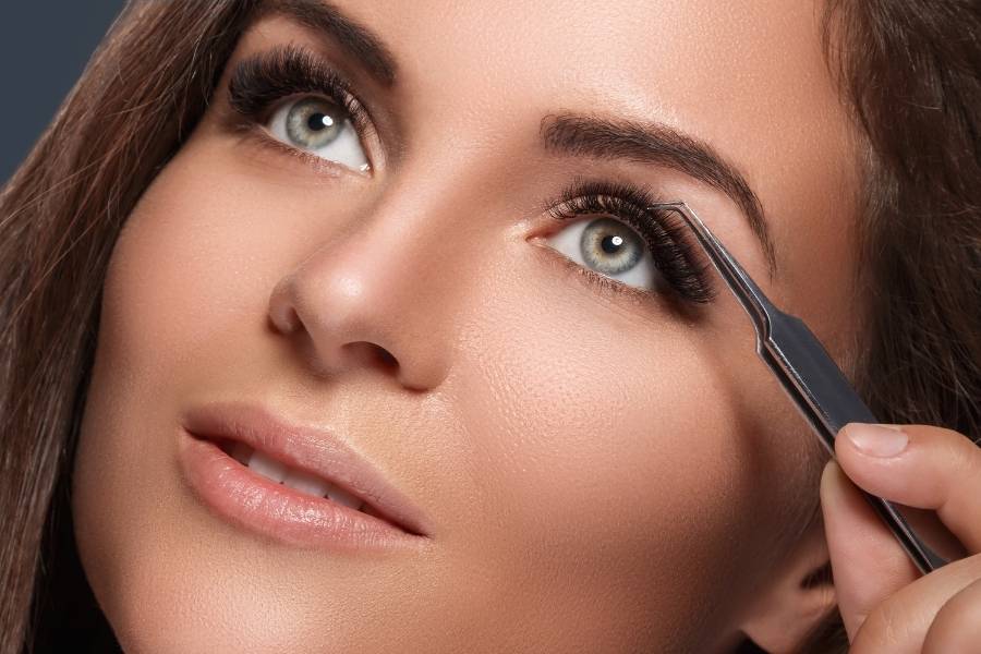Professional eyelash extensions application procedure showing lash artist applying individual extensions with tweezers