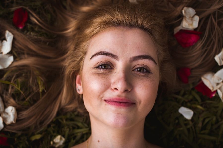 Woman with naturally beautiful lips lying among flower petals demonstrating fuller lips naturally achieved through proper care