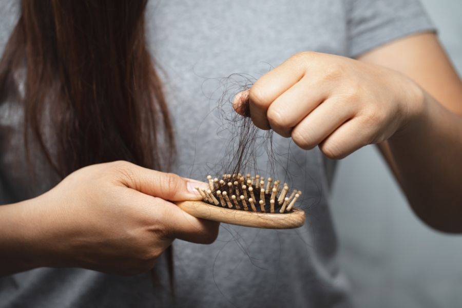 Woman removing excessive hair from brush showing common hair loss problem needing effective solutions