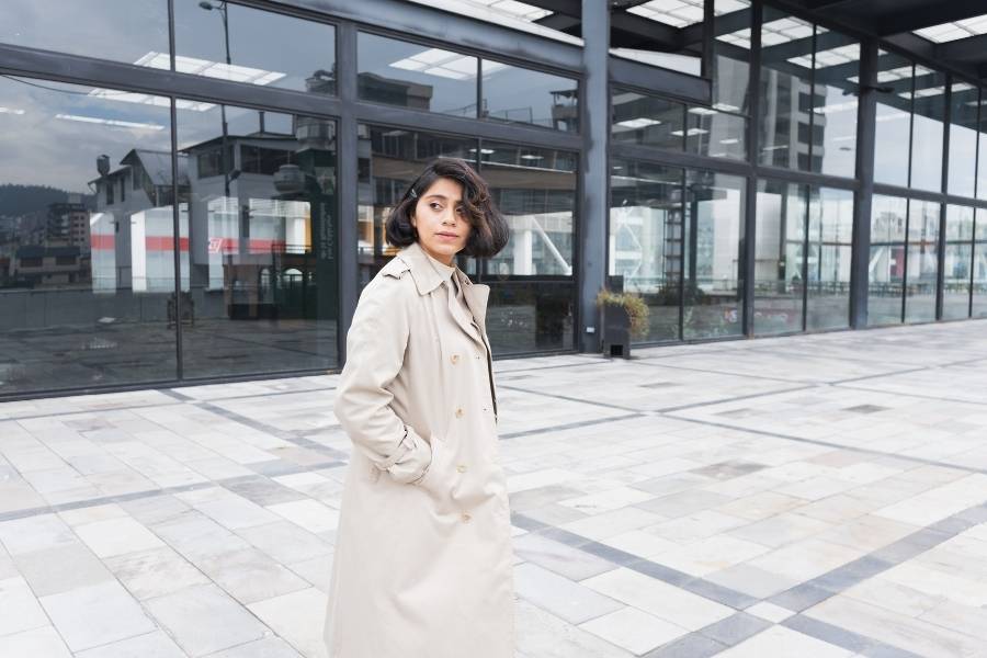 Woman wearing professional outfits with beige trench coat outside modern office building