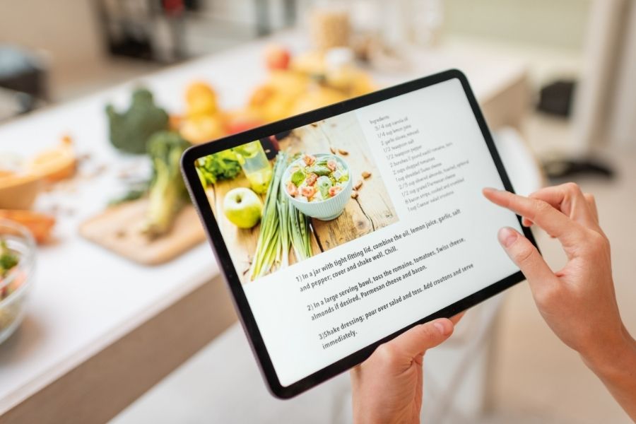 Person following quick kitchen recipes on tablet while preparing fresh ingredients in modern kitchen