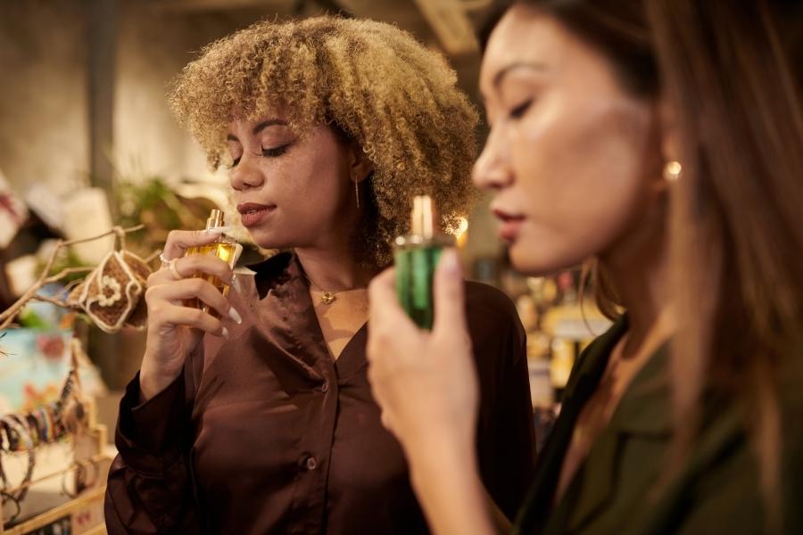 Two women testing seductive women's fragrances in perfume shop with golden lighting