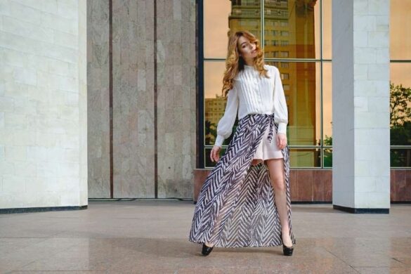 Woman modeling spring fashion trends in white blouse and patterned maxi skirt outside modern building