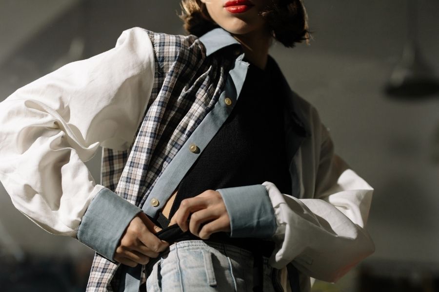 Woman wearing layered stylish outfits with plaid vest, white shirt and blue cardigan in dramatic lighting