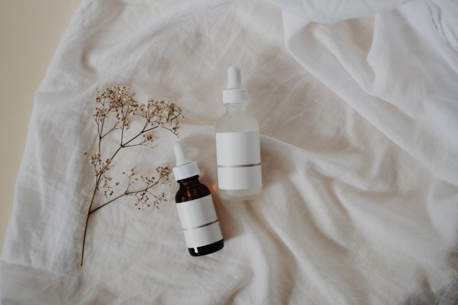 Minimalist clean beauty products display with natural botanical elements on white fabric