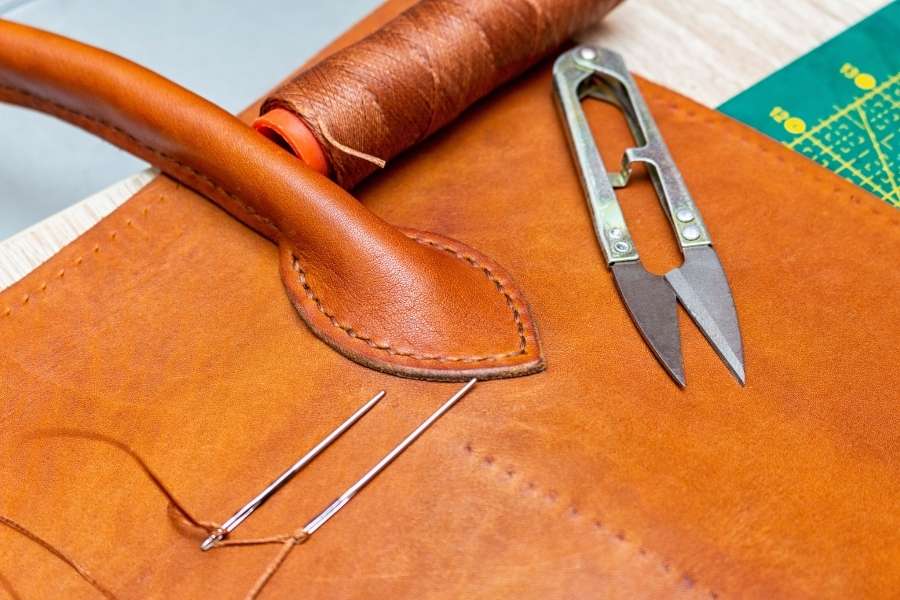 Professional leather crafting tools including scissors and thread on tan leather showing leather care techniques