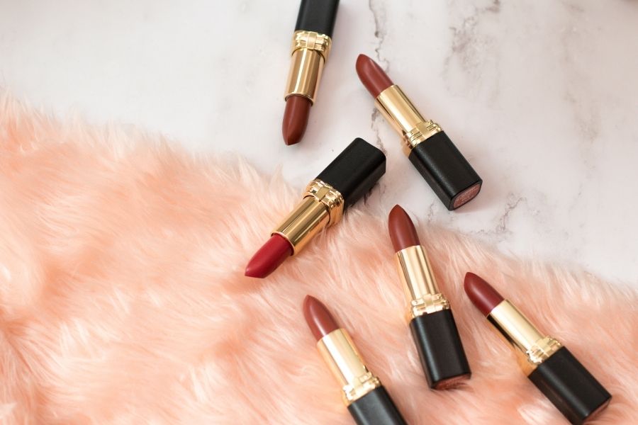 Long-lasting lipstick collection in red and berry shades with gold packaging on marble surface