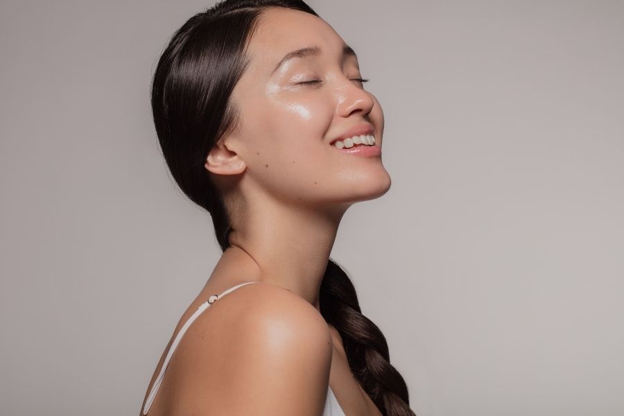 Woman with glowing natural beauty skin smiling with eyes closed showing radiant complexion