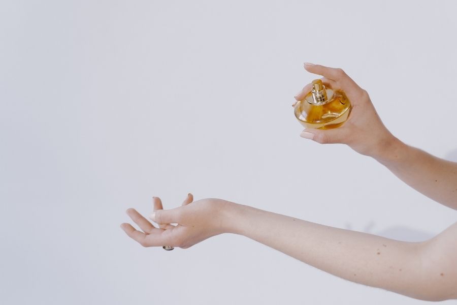 Hand holding elegant perfume bottle preparing to spray signature scent against white background