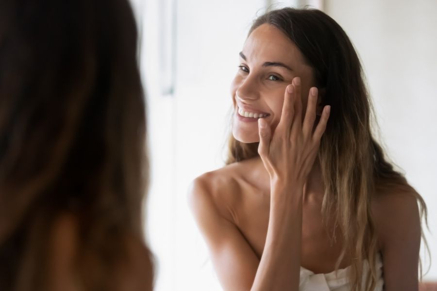 Woman admiring healthy skin in mirror showing proper skincare technique avoiding common skincare mistakes