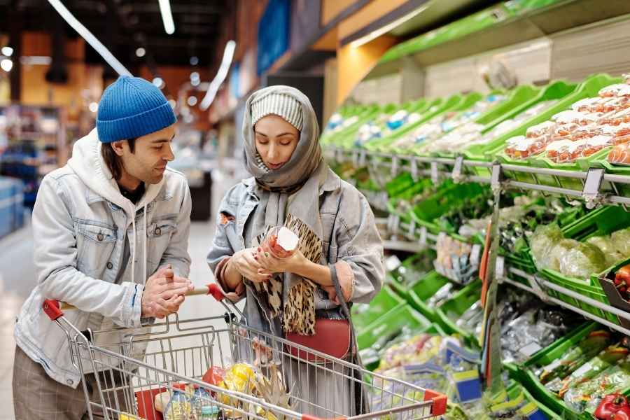 Young couple doing smart shopping together in grocery store produce section comparing products and prices