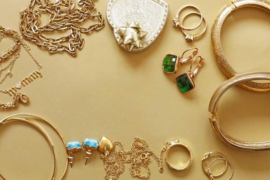 Luxury statement jewelry collection featuring gold chains, emerald earrings and textured bangles on cream background