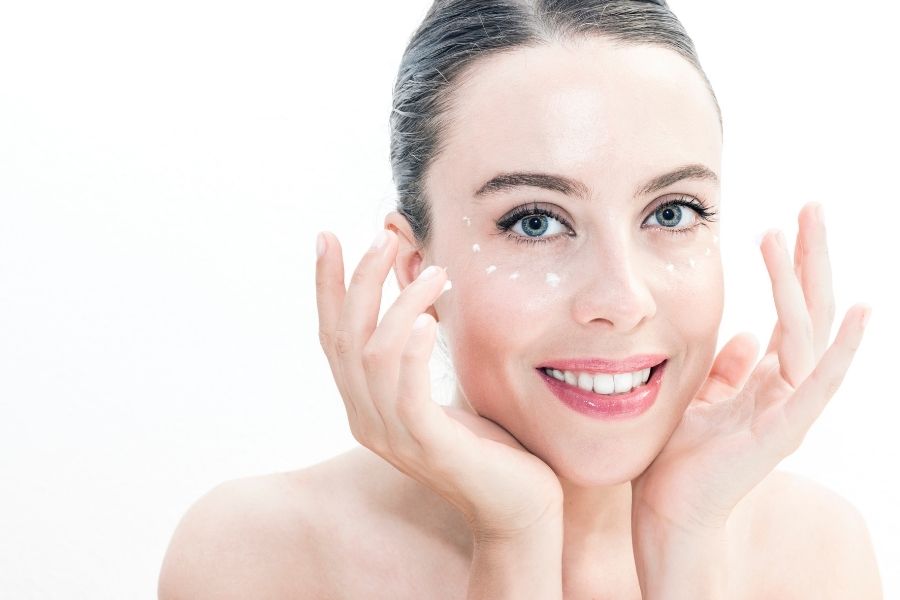 Woman applying easy contouring cream to face with hands against white background