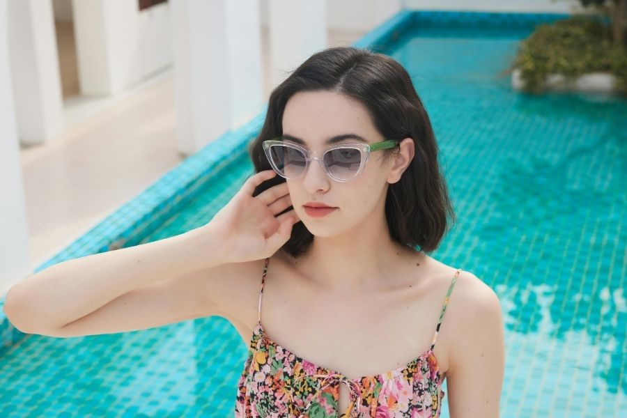 Woman showcasing effortless casual style in floral dress and sunglasses by swimming pool