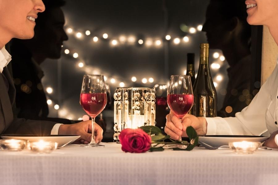 A romantic dinner table with wine, candles, and a red rose
