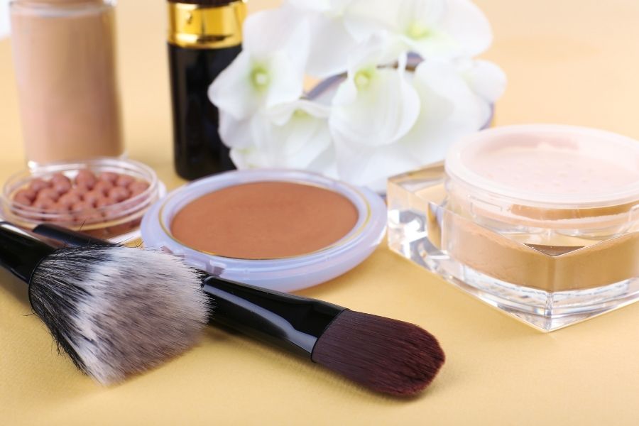 Cream blush compact with makeup brushes and cosmetic products on beige background