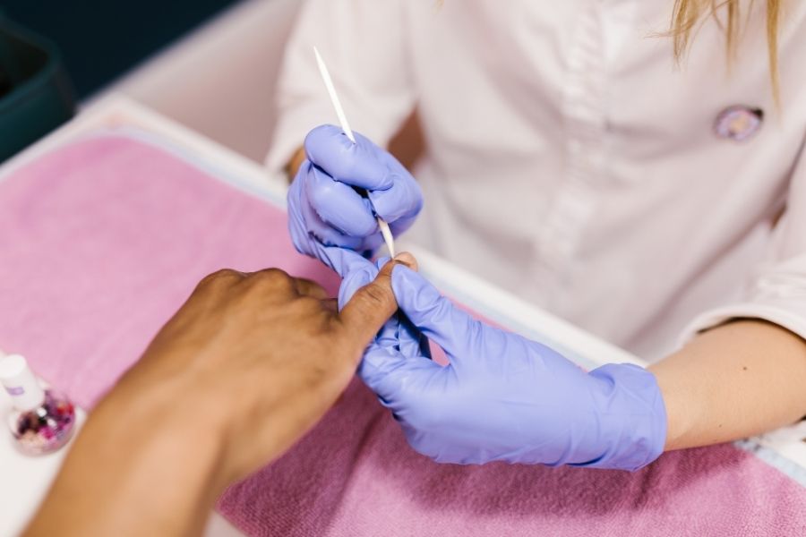 Professional nail technician performing cuticle care routine with cuticle pusher tool