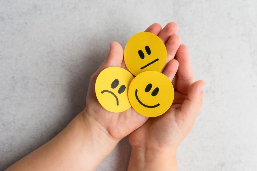 Three yellow emotion faces showing different feelings held in cupped hands to represent emotional intelligence in children
