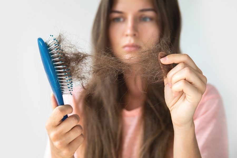 Woman examining stress-related hair loss with clumps of hair caught in blue brush
