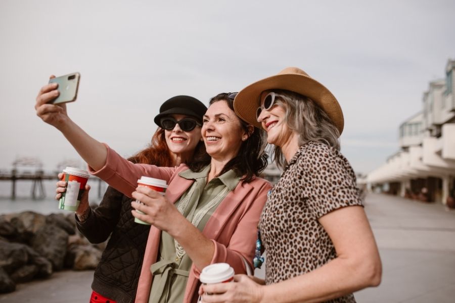 Three stylish women taking selfie outdoors demonstrating importance of heat protectants for hair in sunny weather