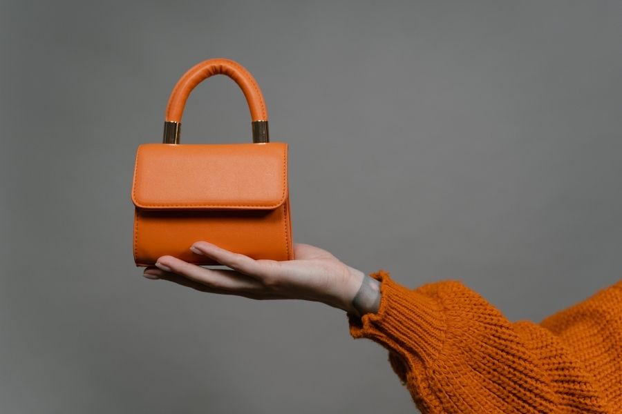 Orange mini investment handbags held in hand wearing matching knit sweater