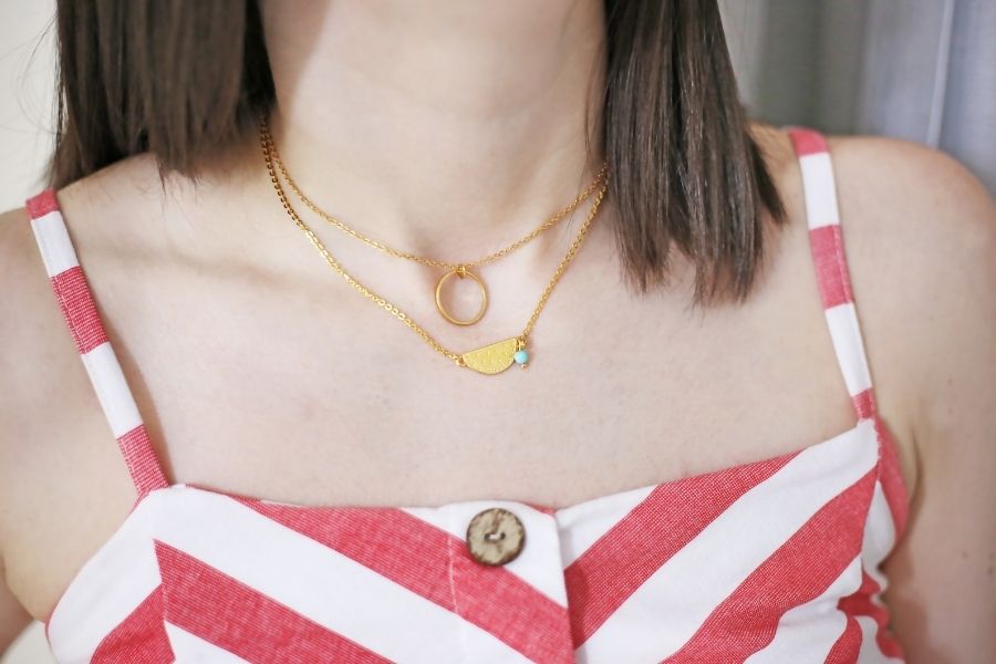 Woman wearing layering delicate necklaces with gold chains and geometric pendants over striped top