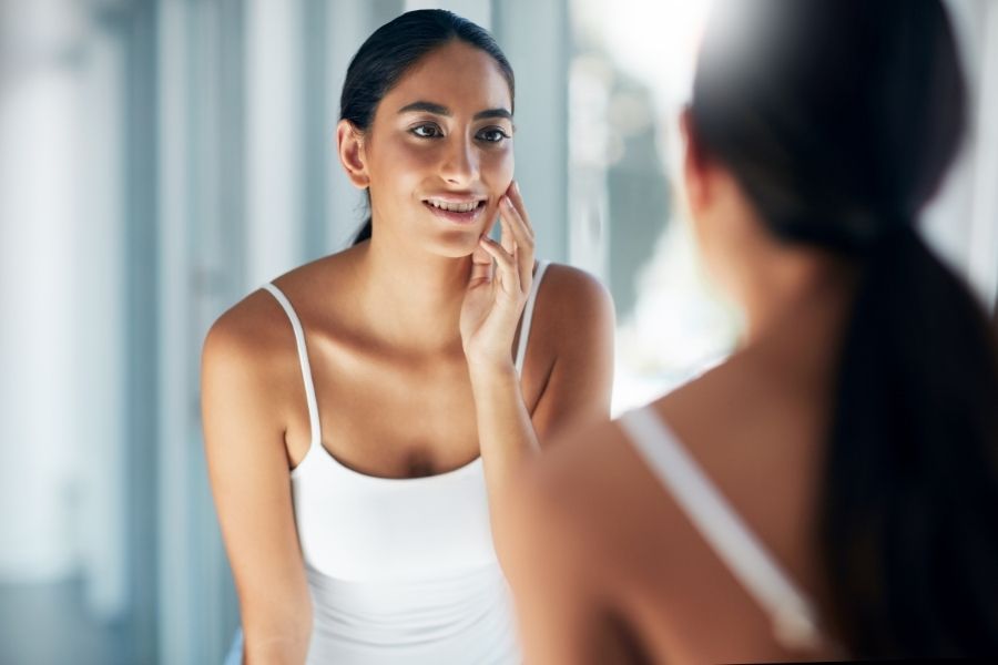 Woman examining her smooth skin in mirror after microneedling at home routine