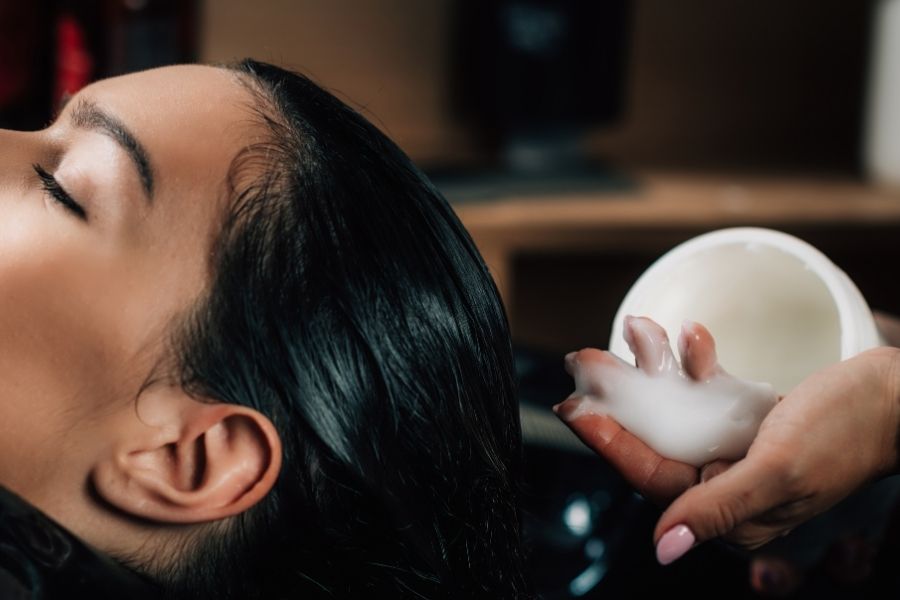 Woman applying premium Olaplex alternatives hair treatment from white bottle for bond repair