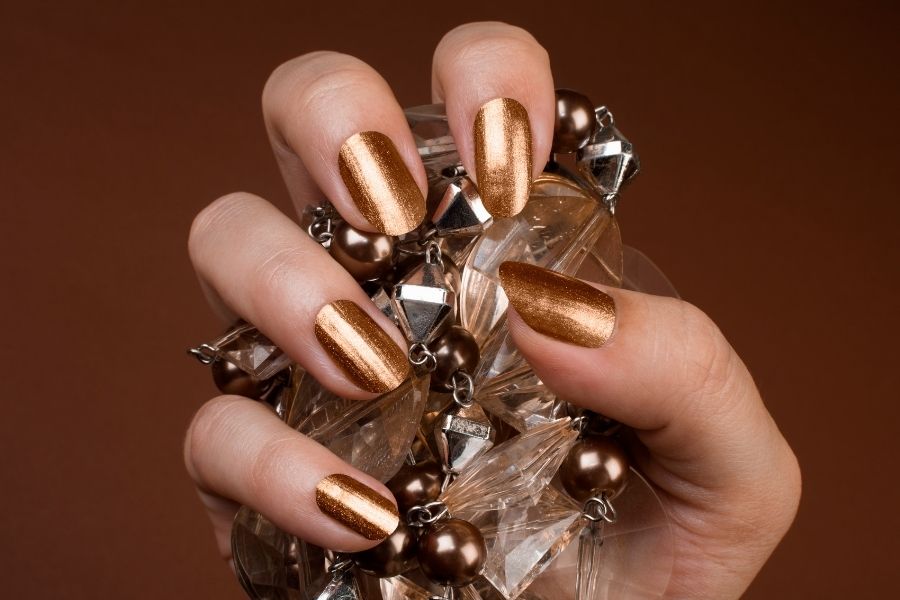 Glamorous bronze metallic press-on nails displayed with decorative crystal jewelry