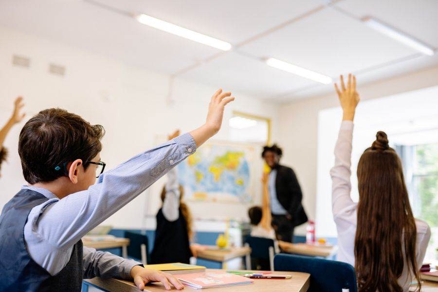 Student eagerly raising hand in classroom demonstrating confidence while raising confident kids through active participation