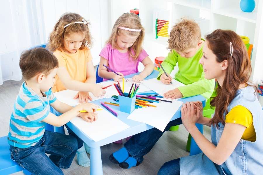 Children enjoying screen-free activities while drawing and crafting together at a white table in a colorful playroom