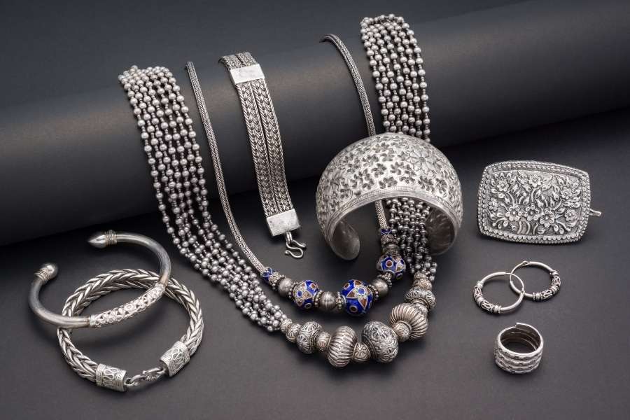 Ornate silver sustainable jewelry collection with intricate metalwork and blue accents on dark surface