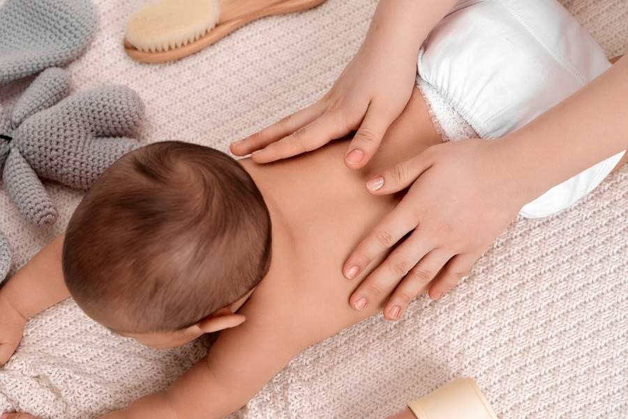 Gentle baby back massage using baby massage oil on soft blanket with natural care products