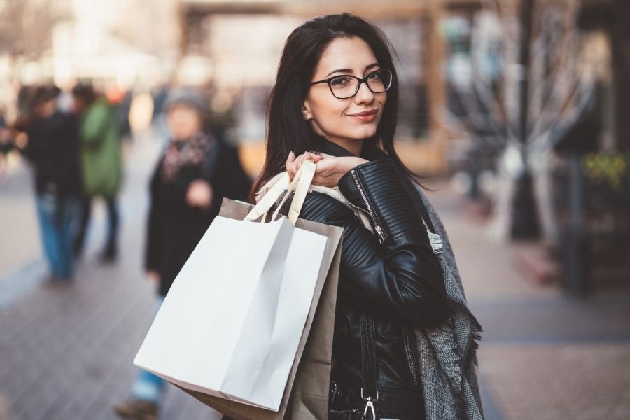 Stylish woman with glasses carrying shopping bags during Black Friday beauty shopping spree