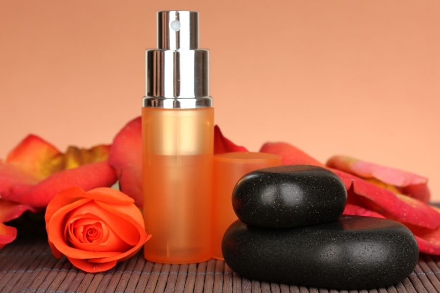 Orange body mist bottle with spa stones and rose petals on bamboo mat