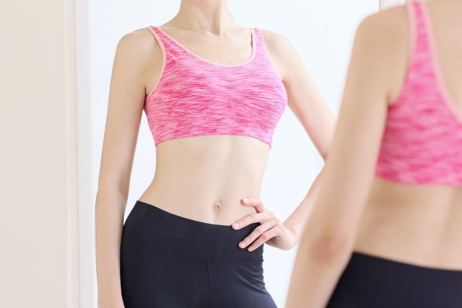 Woman in pink sports bra demonstrating proper bra fitting in front of mirror