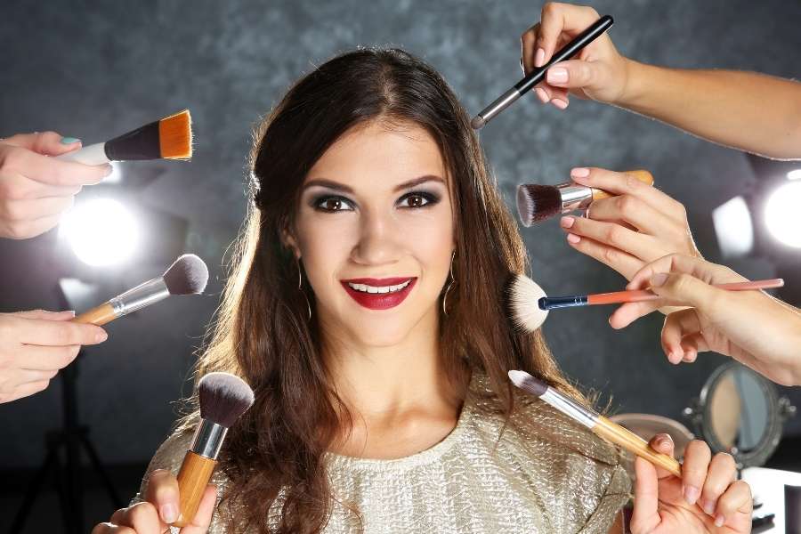 Professional bridal makeup artist applying makeup to smiling bride with multiple brushes and tools