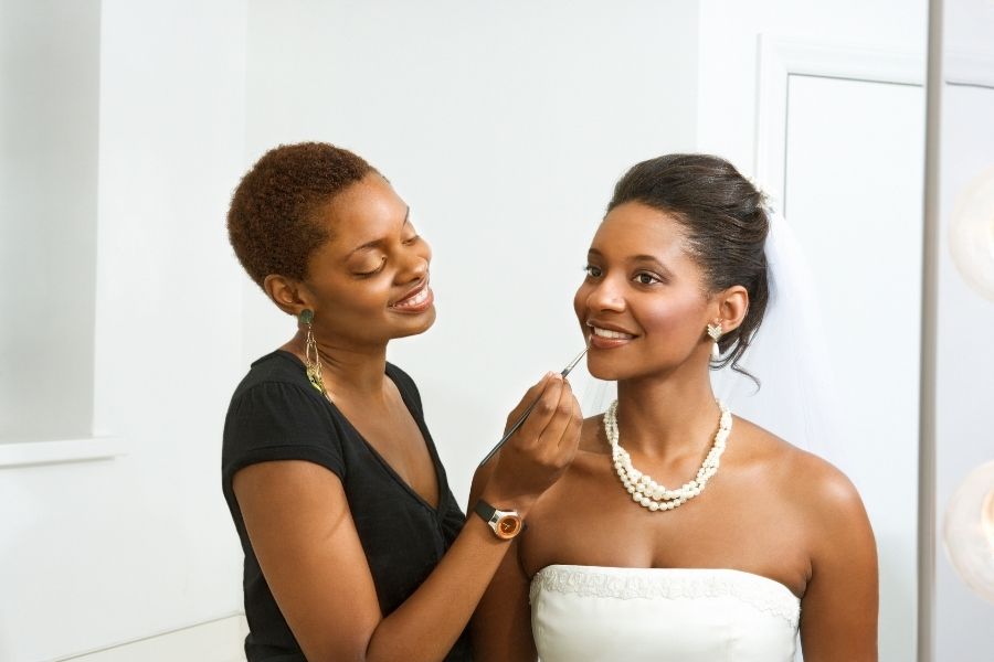 Professional makeup artist applying bridesmaid makeup with elegant pearl accessories in bridal suite